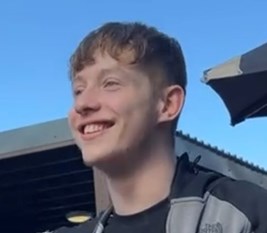 24-year-old man smiling wearing a grey and black top