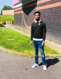 40-year-old man standing outside with building and grass in the background wearing dark jumper, jeans and trainers