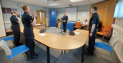 Three Police Scotland probationary constables in black uniforms standing with backs to camera making their oath of office in Inverness, watched by a female senior officer in formal uniform with white shirt, cravat and black trousers.