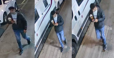 CCTV image showing a man wearing dark trainers, blue jeans, a white t-shirt and dark jacket walking along a street.