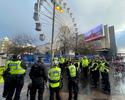 Around 28 officers in uniform standing in group at square in city with ferris wheel in front of them