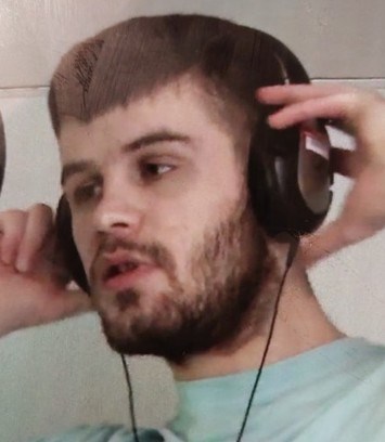 Image shows a man. He has dark hair and dark facial hair.