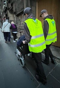 Two Police Scotland Youth Volunteers pictured helping push a person in a wheelchair in Edinburgh