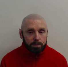 James clacher - white man in 50s with shaved head and dark beard wearing red zip up top
