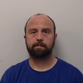 40-year-old white man with brown hair and facial hair wearing a blue jumper