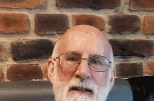 The image shows missing person Roderick MacPherson. He has a white beard and is wearing glasses sitting in front a brick wall