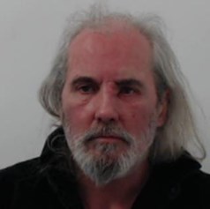 White man with grey/white hair and grey/white beard wearing a dark coloured top.