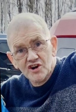 Picture of a bald man in his 50s, wearing glasses and a blue striped jumper, with his mouth open as if he is speaking.