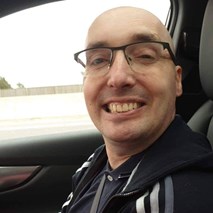 43-year-old white man. Bald, wearing glasses and dark coloured top