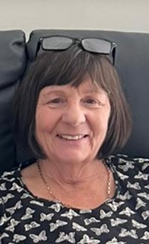 71-year-old woman with dark hair wearing glasses on her head and a top with white pattern