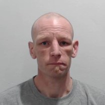 Mugshot of a white man in his 40s, bald, wearing a grey top