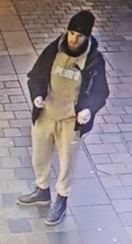 Image of a man aged between 25-35 years of medium build with a red/blonde toned beard.  He is wearing a black beanie hat, black rain jacket, beige Puma track suit and brown boots.