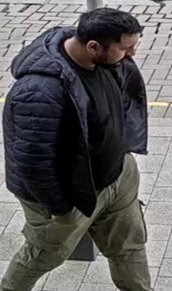 Man with black hair and beard. He is wearing a black top and jacket and trousers