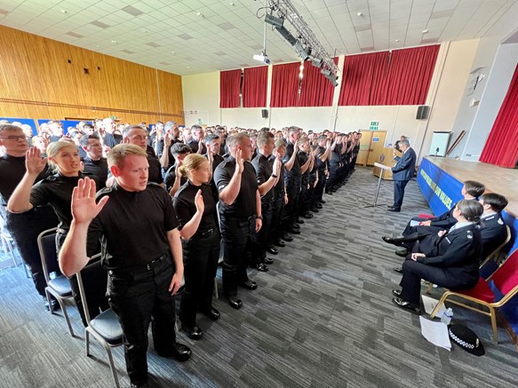 A group of Police Scotland officers in black uniform with right hands raised swear the Oath of Office at Police Scotland Headquarters, Tulliallan.