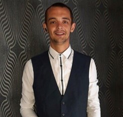 Image of man with short dark hair wearing long sleeved white shirt and dark coloured waistcoat