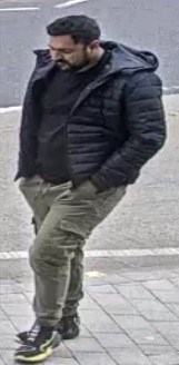 Man with black hair and beard. He is wearing a black top and jacket and trousers