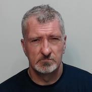 Pictured is a white male. He has grey hair and a grey goatee beard. He is wearing a dark coloured top.
