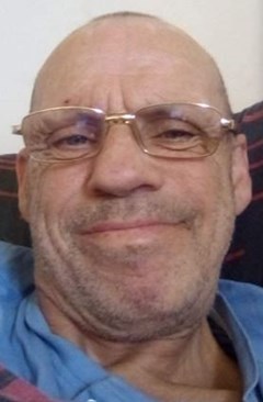 White man in 60s smiling, wearing metal-framed glasses and a blue t-shirt.