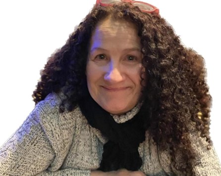 62-year-old white woman with long, curly brown hair wearing a grey jumper